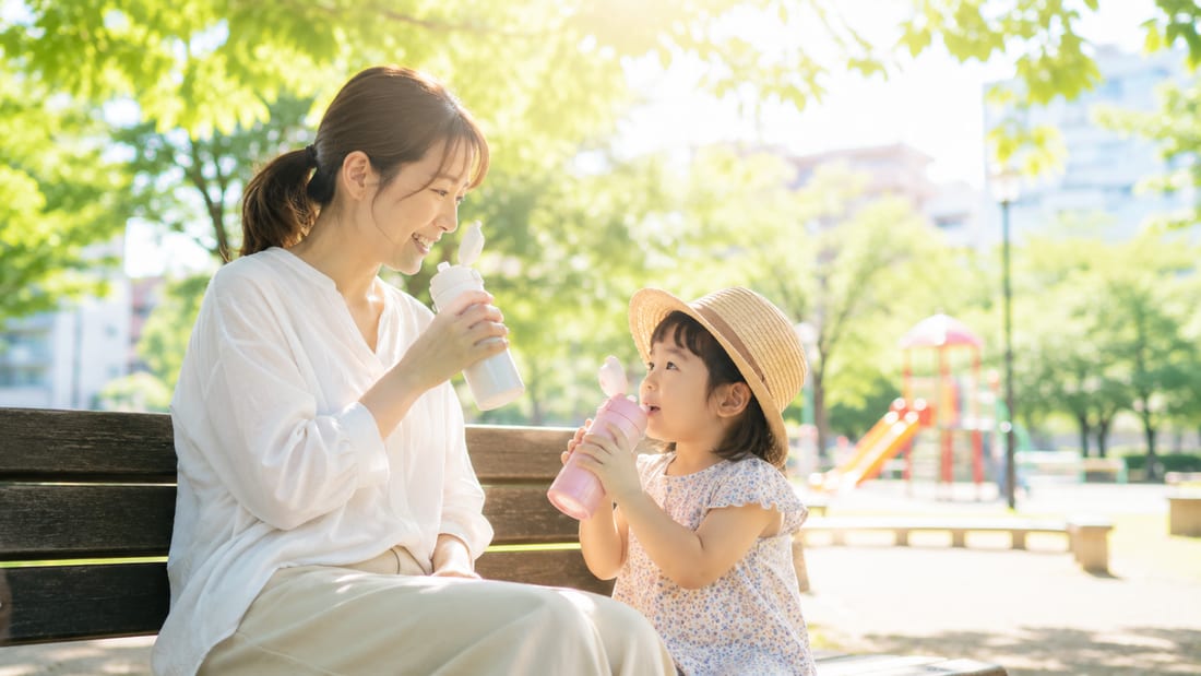夏の公園で親子が水分補給をしながら休憩する様子