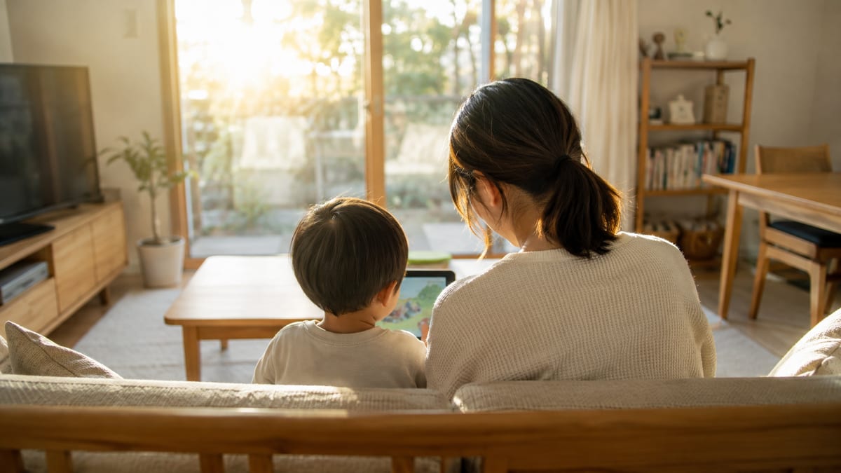 夕方のリビングで、ソファに並んでタブレットを見る親子の後ろ姿