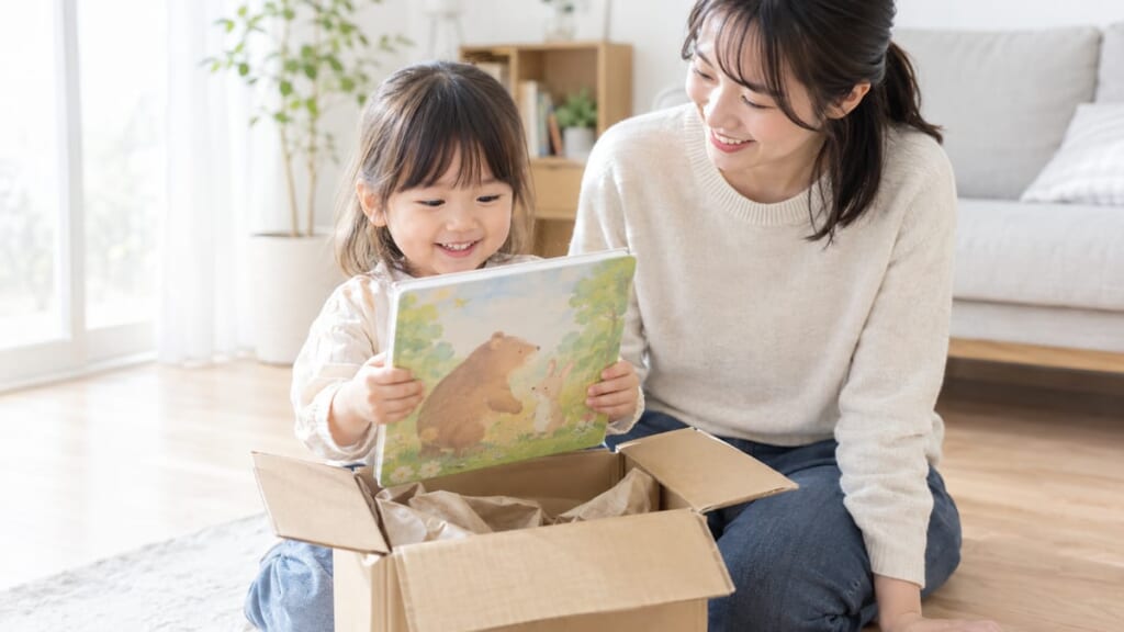 届いた段ボール箱から絵本を取り出してよろこぶ子どもとお母さん