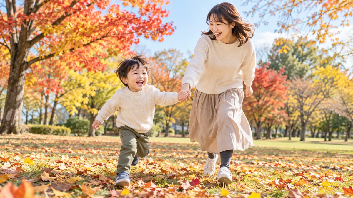 秋の紅葉した公園で、落ち葉の上を手をつないで走るお母さんと男の子