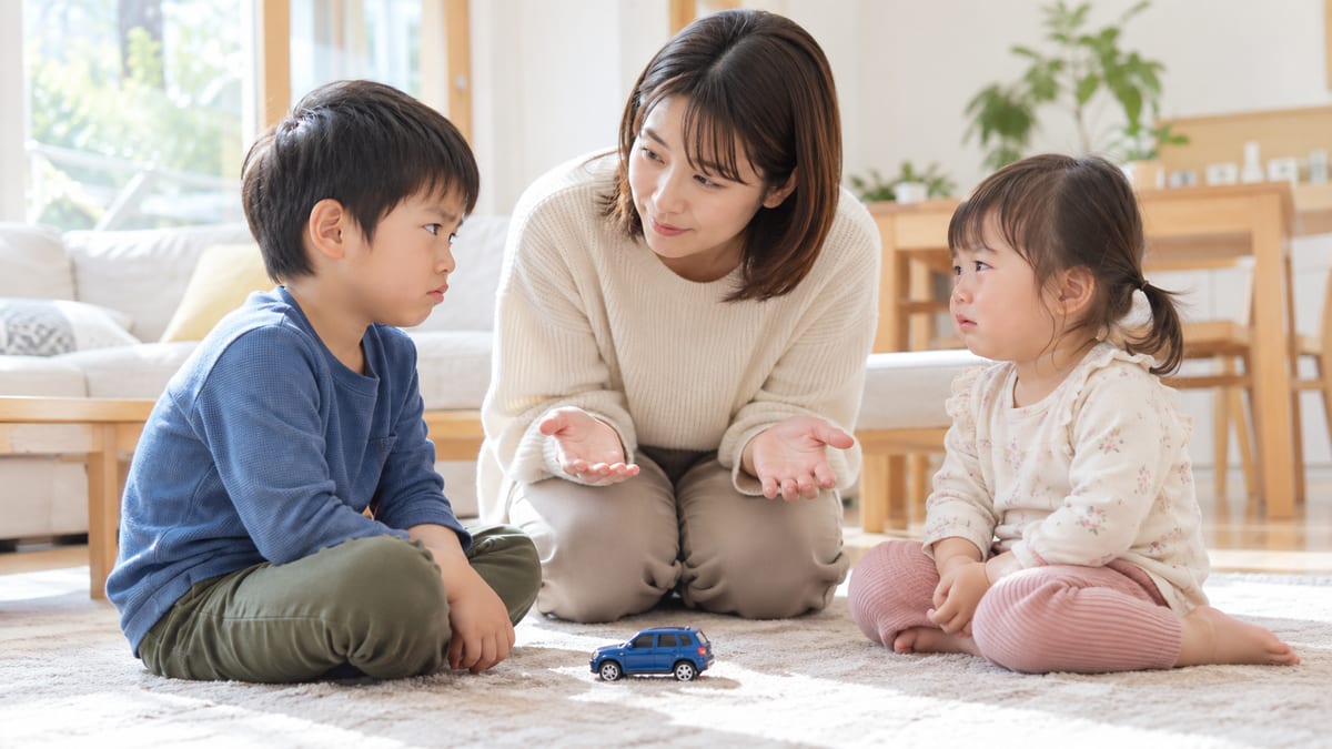 リビングの床で、きょうだいと目線を合わせて話を聞くお母さん