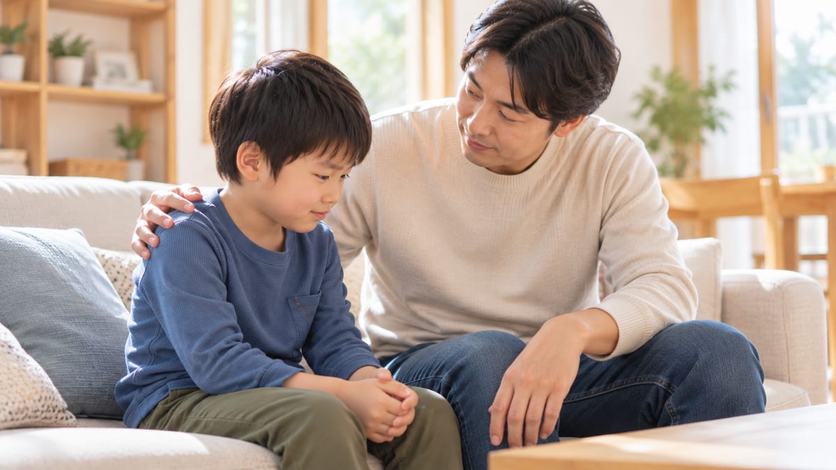 ソファで男の子の肩に手をおいて話をするお父さん